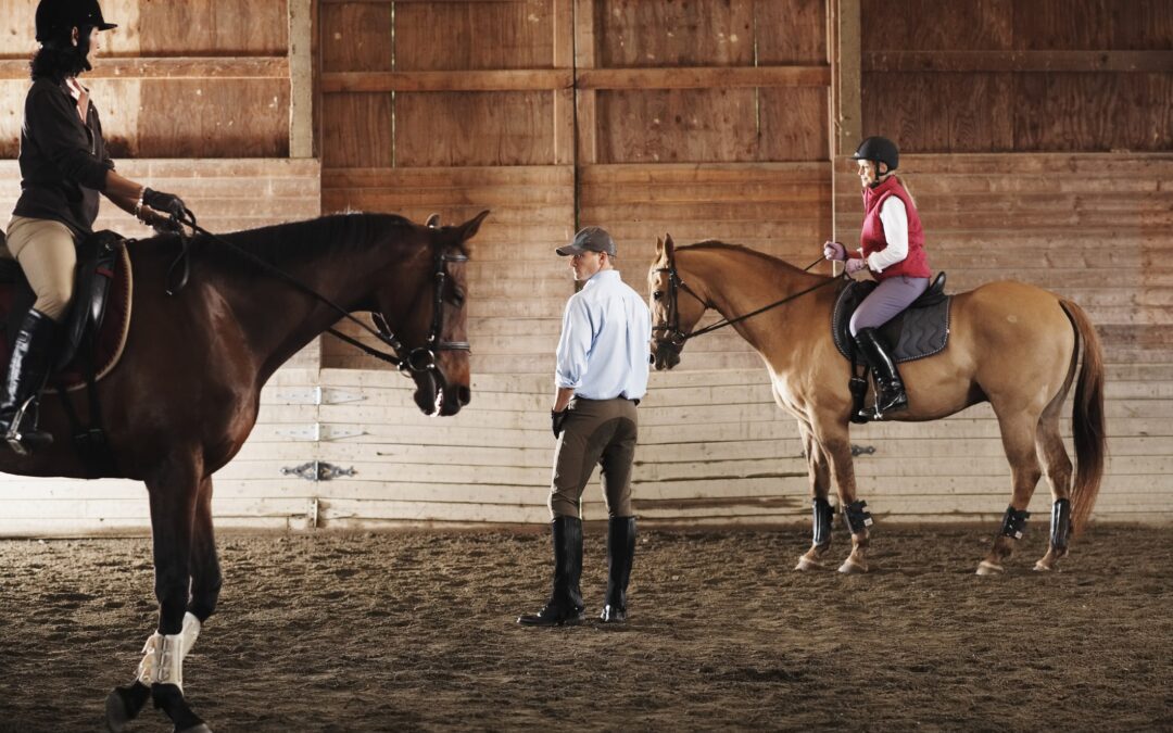 Young man standing between to riders and their horses in a training stable