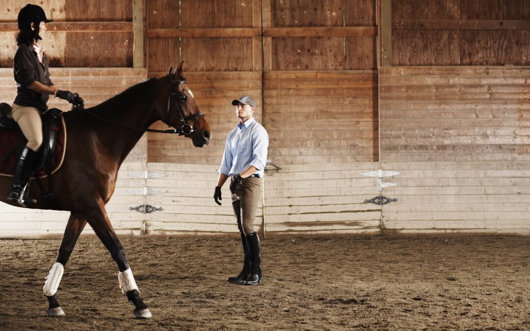 Young man standing next to rider and her horse in a training stable